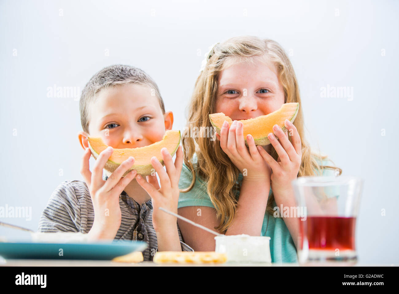 Enfants (6-7, 8-9) eating cantaloupe pour le petit déjeuner Banque D'Images