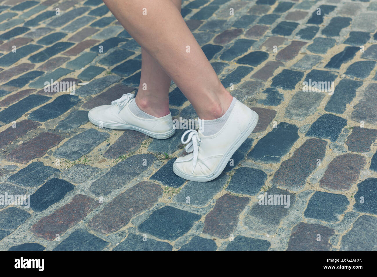 Les jambes et les pieds d'une jeune femme debout sur une rue pavée Banque D'Images