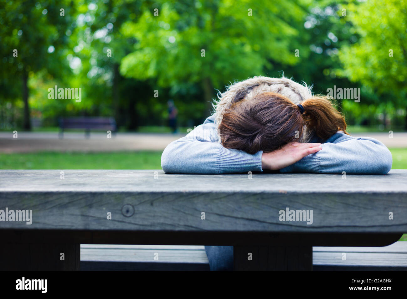Une triste jeune femme avec sa tête reposant sur ses mains à une table dans le parc Banque D'Images