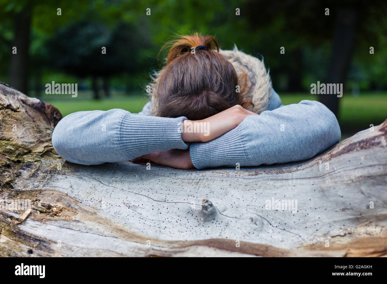 Une jeune femme triste repose sa tête sur un tronc d'arbre dans le parc Banque D'Images