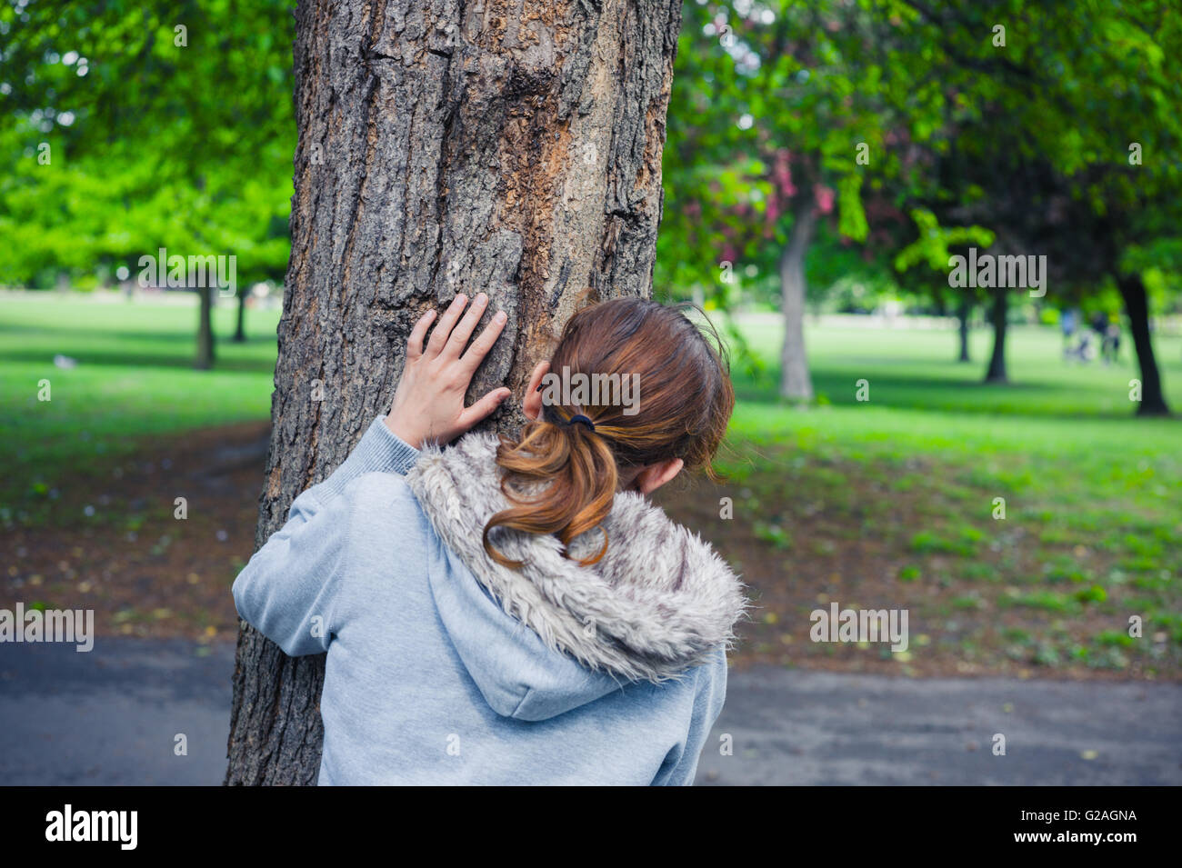 Une jeune femme se cache derrière un arbre dans le parc Banque D'Images