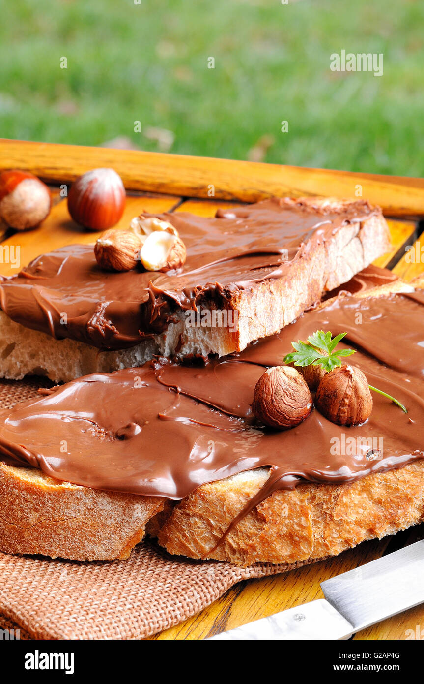 Deux tranches de pain avec la crème au chocolat et noisettes sur une table en bois à l'extérieur. Composition verticale. Banque D'Images