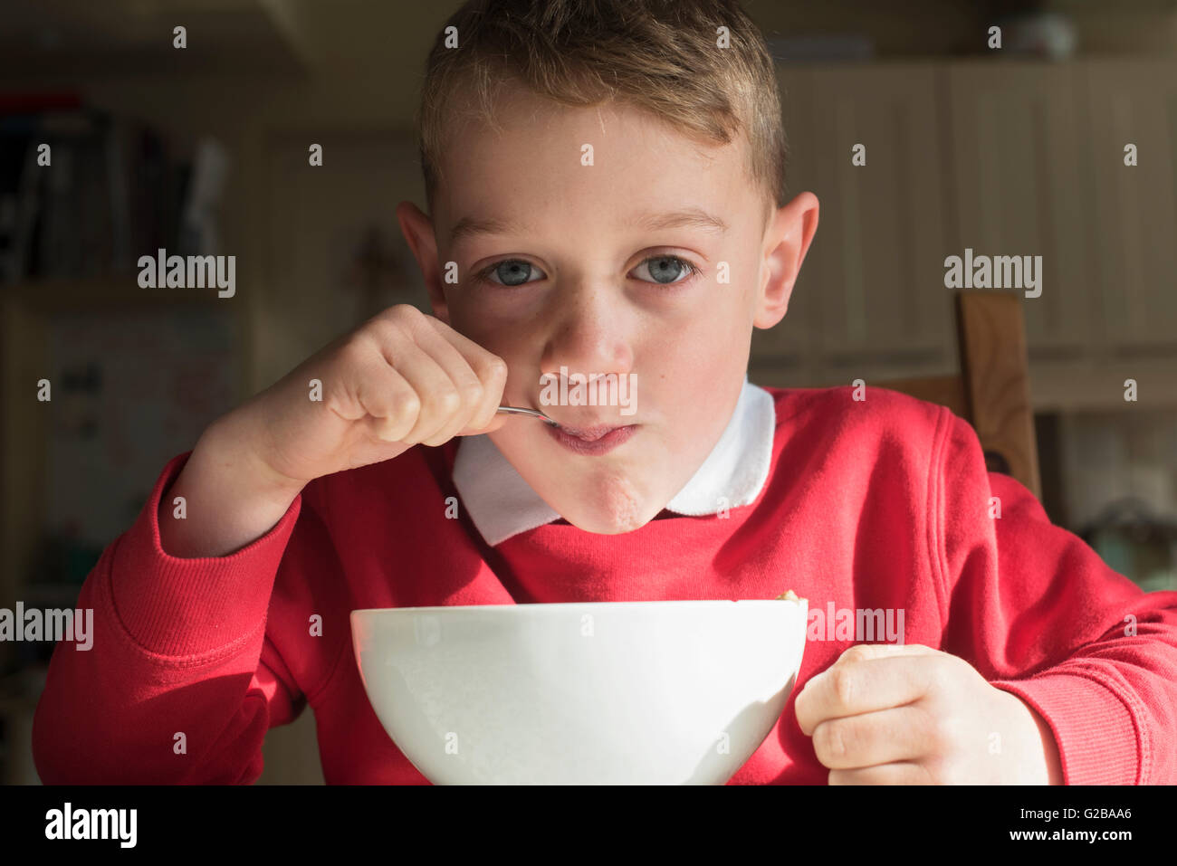 Cavalier rouge enfant en prenant un petit déjeuner à partir de la boule blanche avant d'aller à l'école fond sombre un contact visuel avec l'horizontale de l'appareil photo Banque D'Images