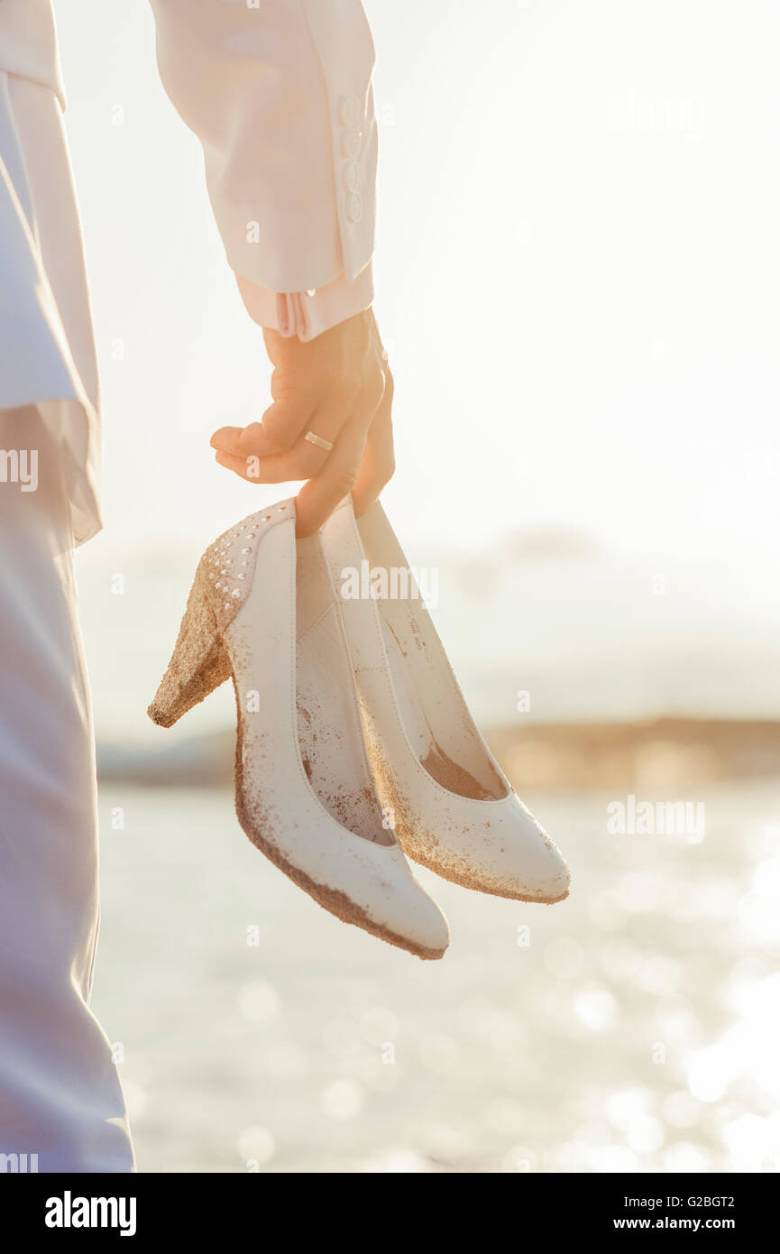 Man holding white stiletto shoes, sur une plage Banque D'Images