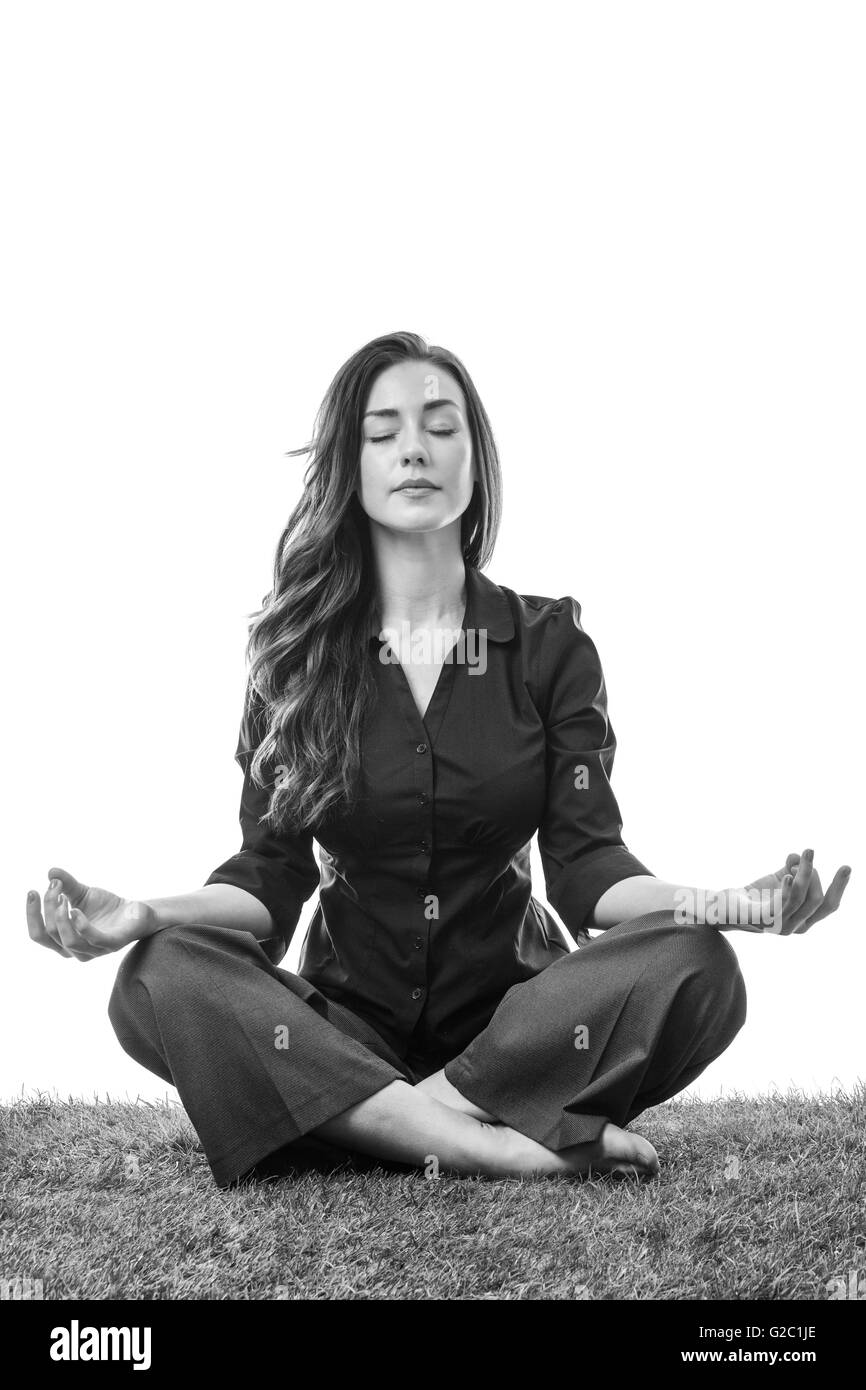 Jolie jeune femme d'affaires en costume, assis sur l'herbe dans un yoga pose les jambes croisées, avec ses bras reposant sur ses genoux, paumes u Banque D'Images
