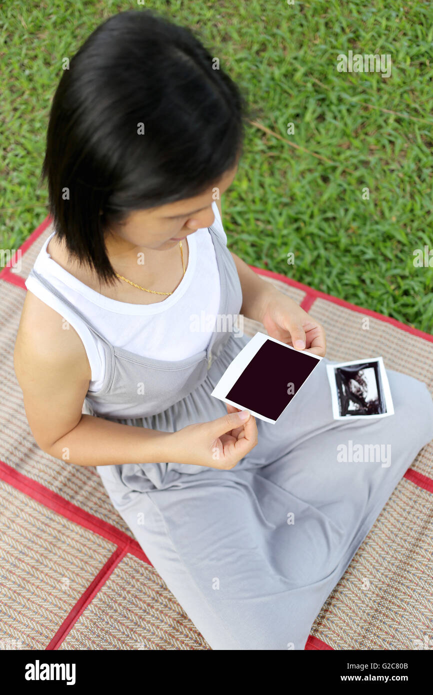 Les femmes enceintes asiatiques voir film d'échographie photo bébé sur son ventre dans la main au jardin. Banque D'Images
