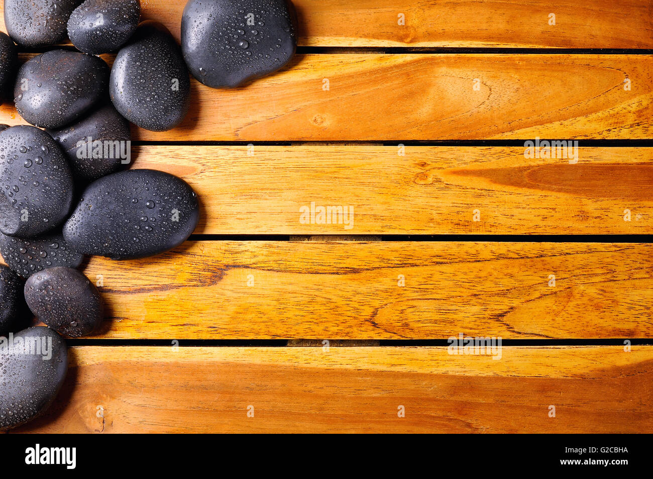 Les pierres noires avec de l'eau tombe dans le coin supérieur gauche sur des lattes de bois. Sauna et massage concept. Composition horizontale. Haut Banque D'Images