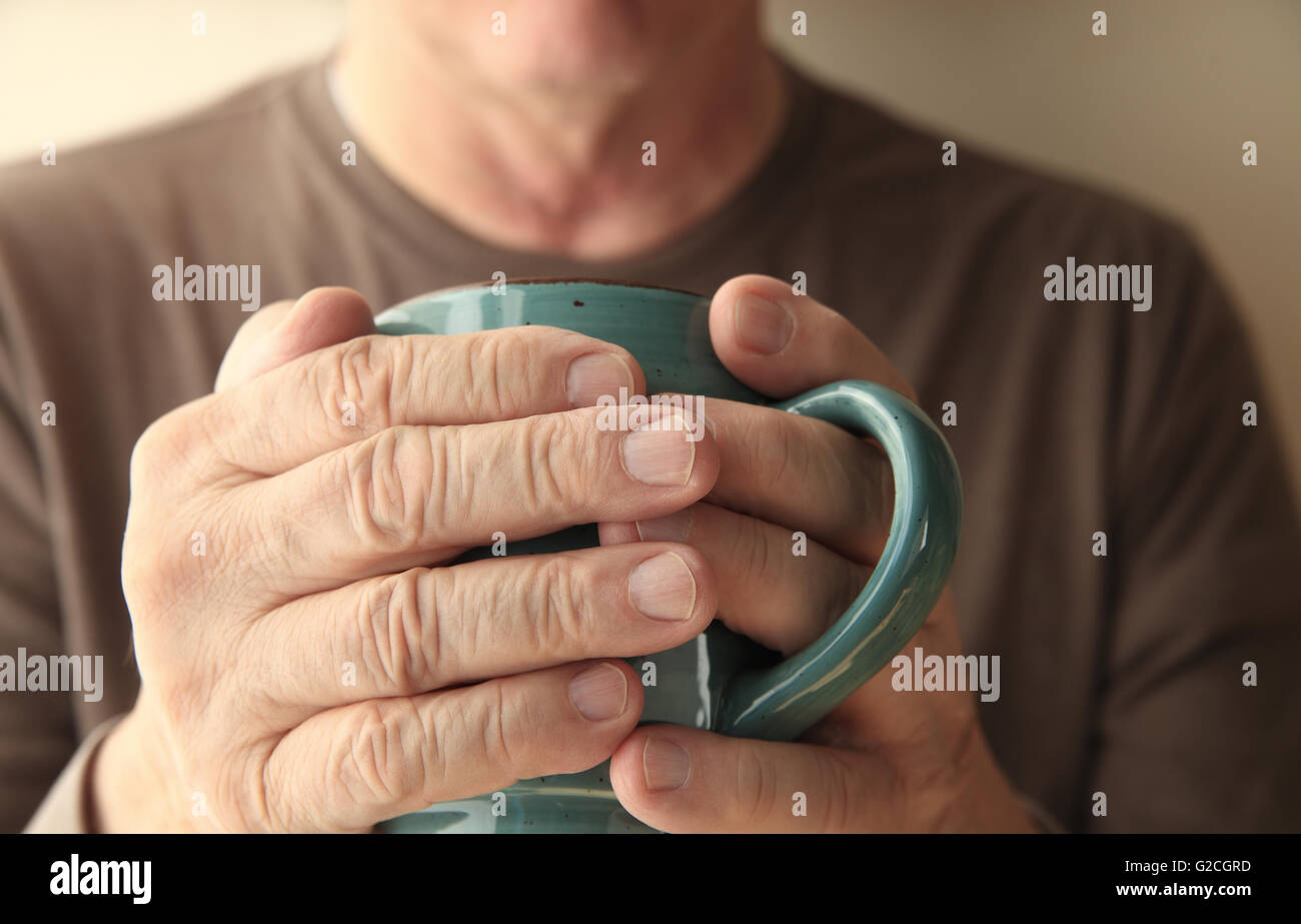 Homme plus âgé se réchauffe ses mains avec une tasse de café chaud. Banque D'Images