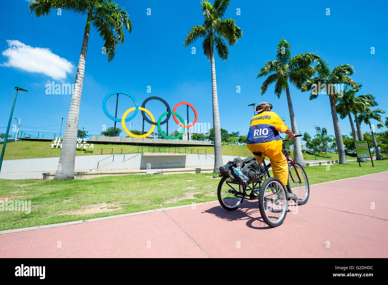 RIO DE JANEIRO - le 18 mars 2016 : un travailleur pour la COMLURB, entreprise de nettoyage municipal, en face de tricycle en anneaux olympiques. Banque D'Images