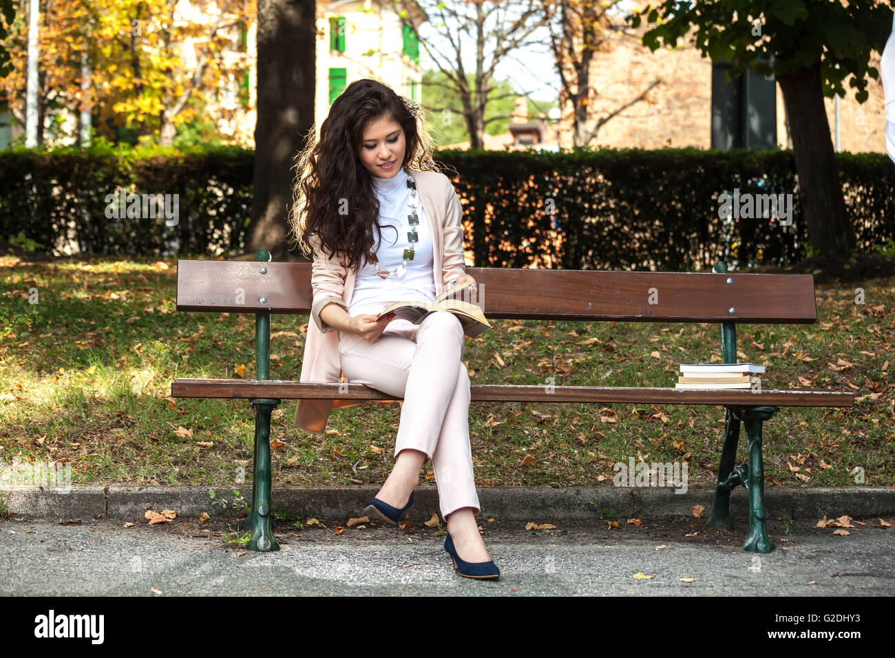 Jeune femme souriante asiatique et assis sur un banc, lisant un livre dans le parc Banque D'Images