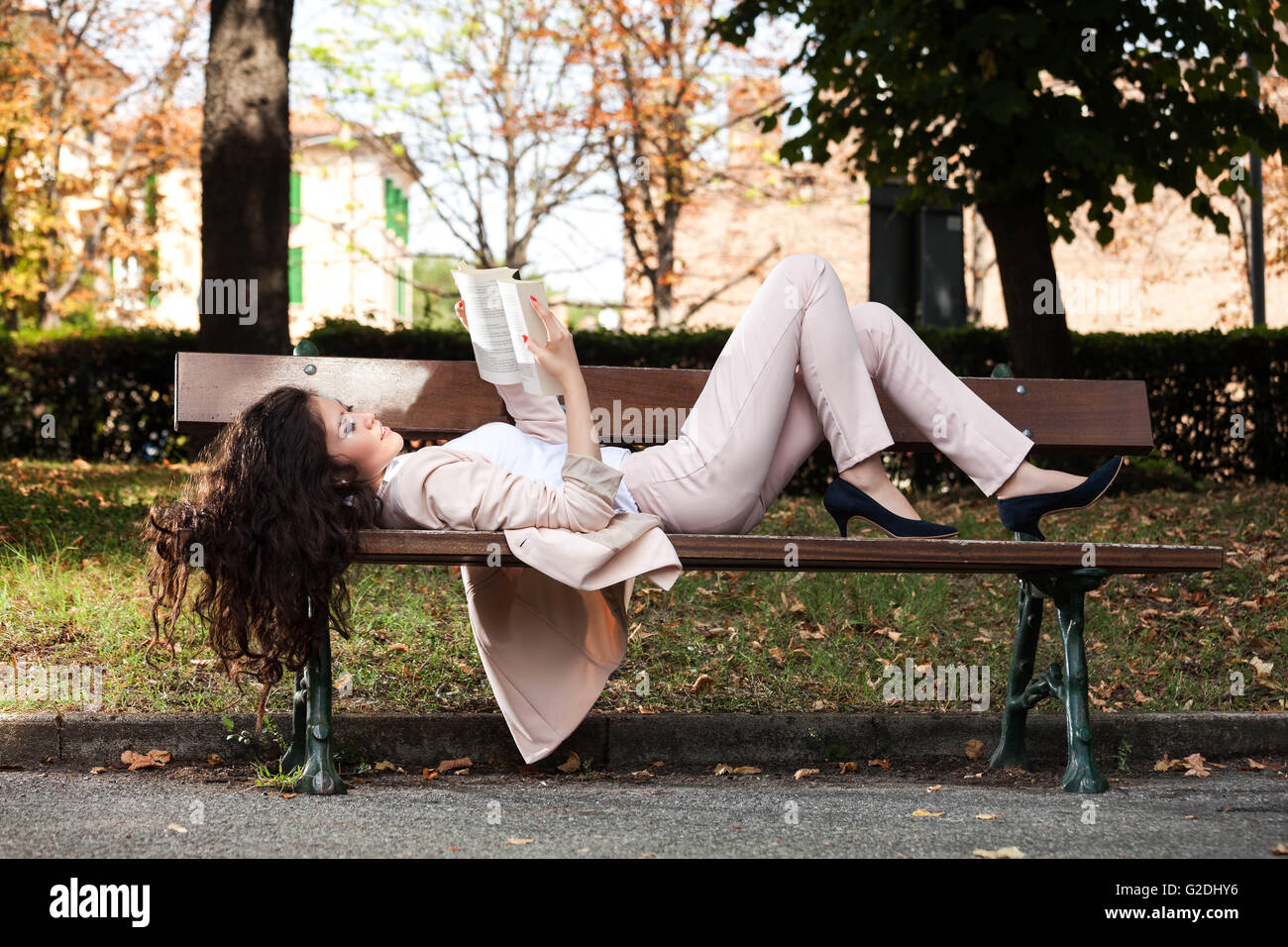 Jeune femme souriante asiatique et allongé sur un banc de la lecture d'un livre dans le parc Banque D'Images