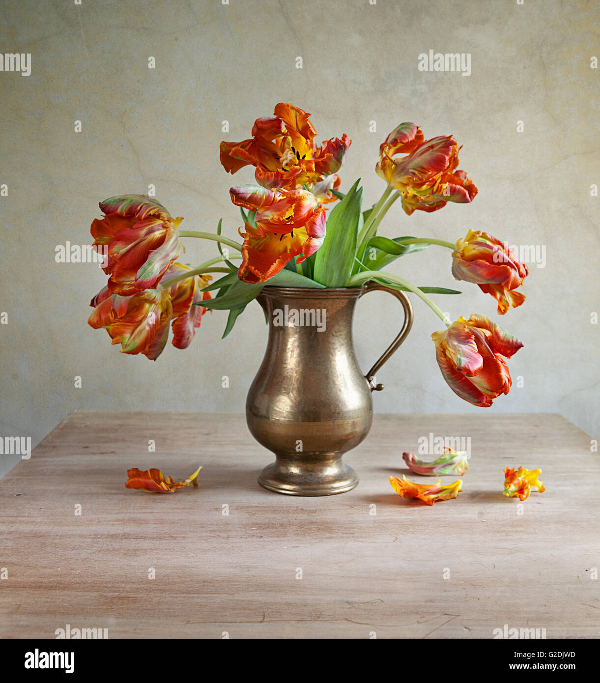 Orange-ornementale tulipes jaunes dans une antique metal verseuse à pétales tombés sur la vieille table en bois Banque D'Images