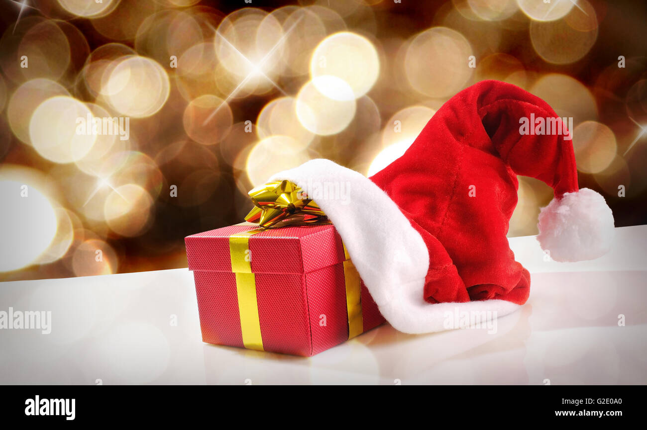 Santa Claus hat avec cadeau rouge sur blanc table méthacrylate. Flou d'or à l'arrière-plan. Vue avant et diagonal. L'horizontale Banque D'Images