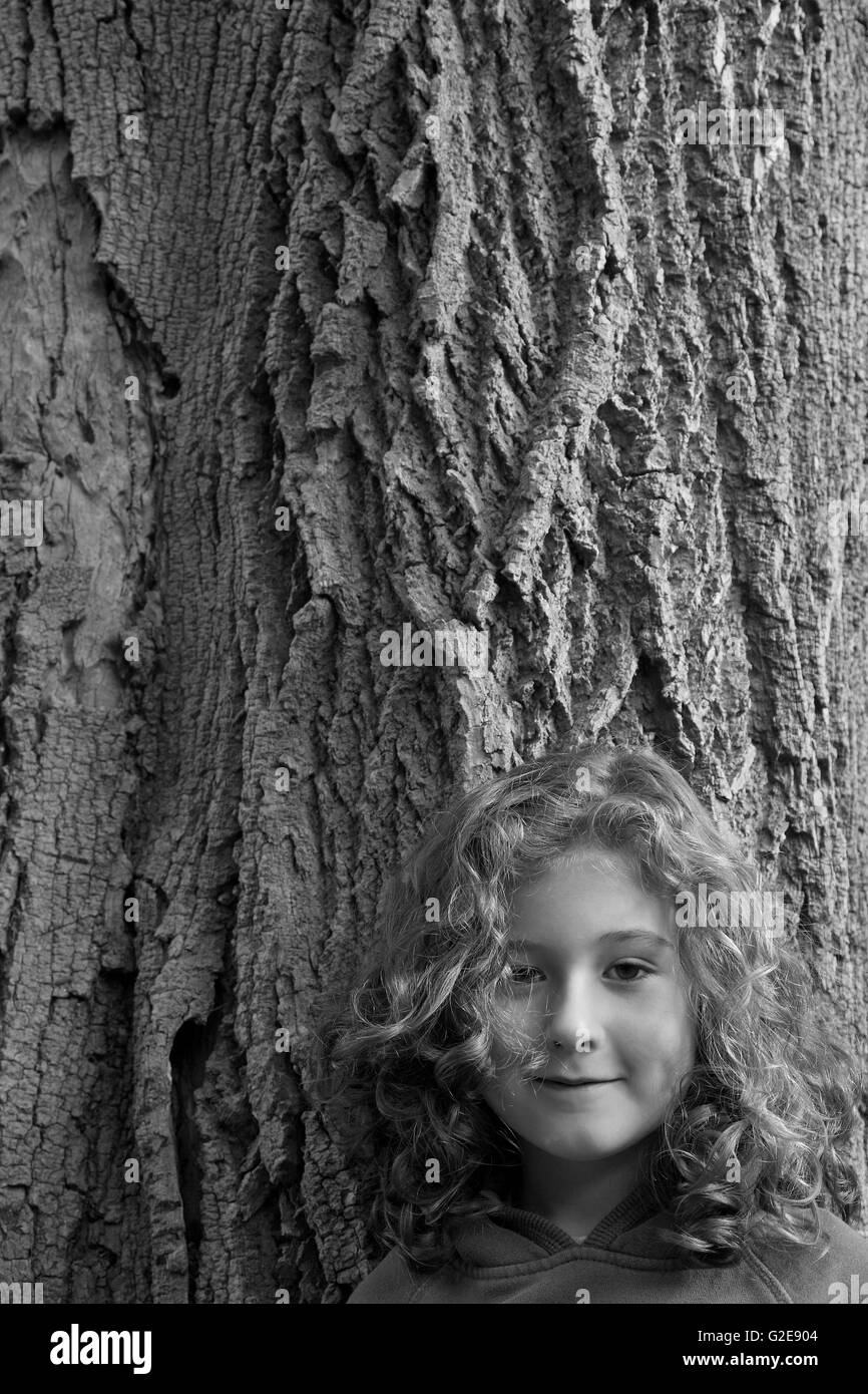 Smiling Girl avec des cheveux bouclés debout contre un tronc d'arbre Banque D'Images