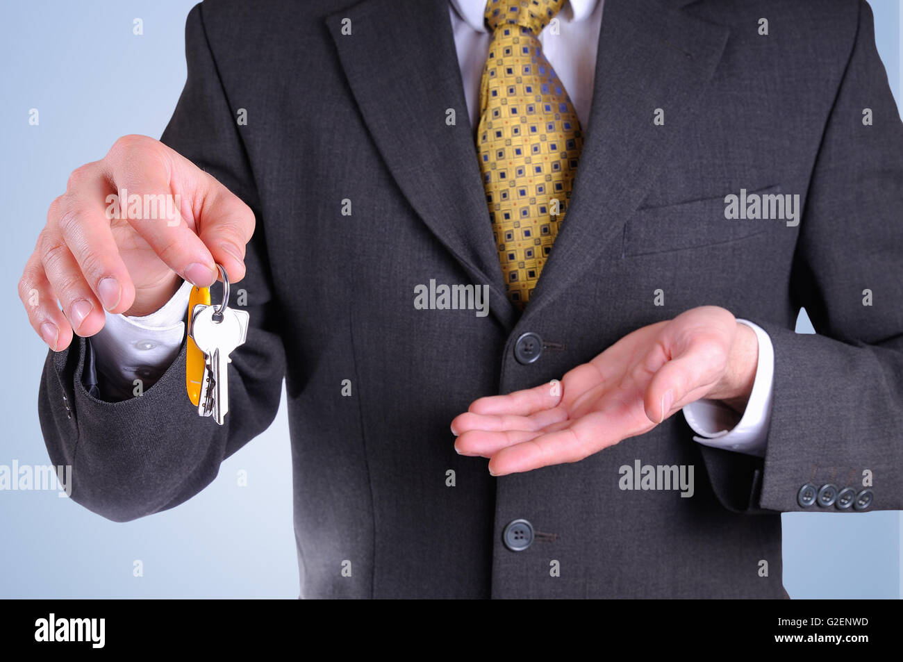 La moitié avant-corps de l'agent commercial le port d'un costume gris foncé remise des clés pour l'achat d'une maison avec fond bleu je Banque D'Images