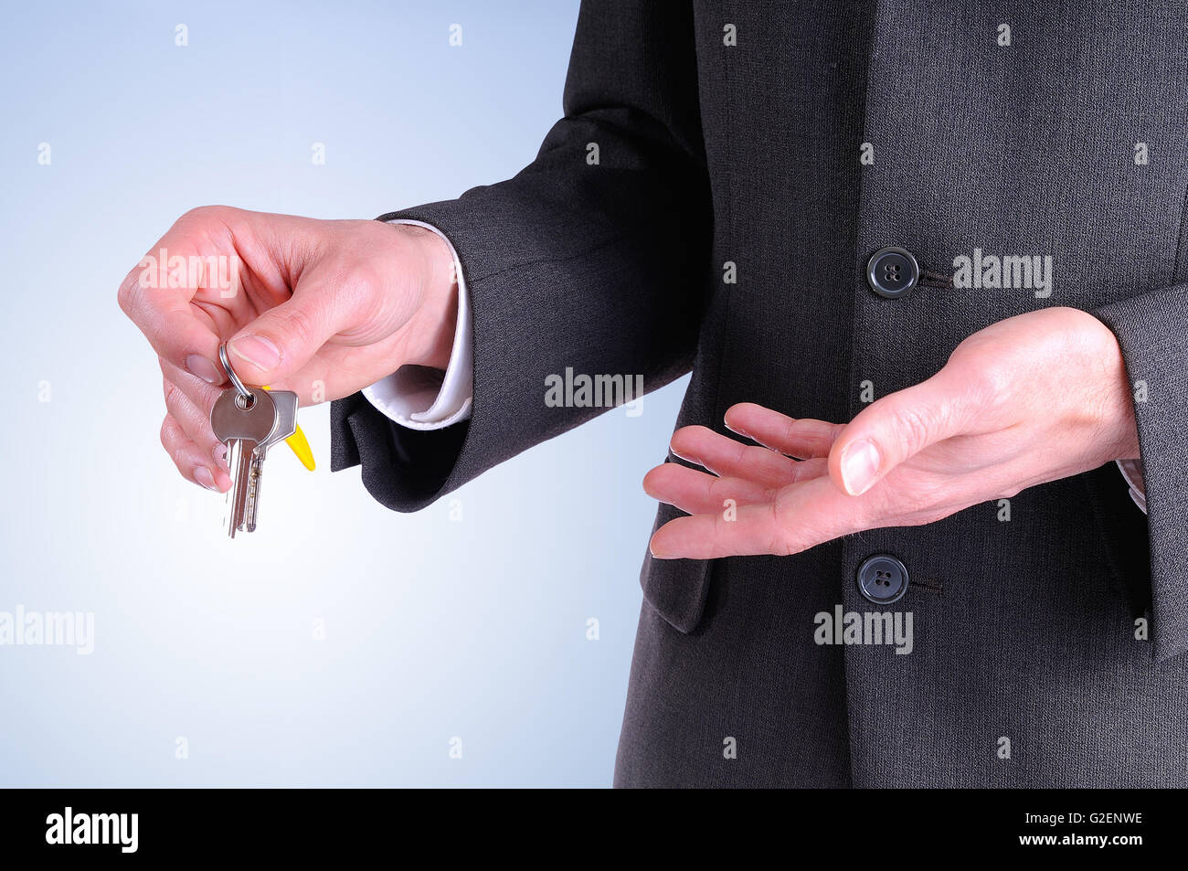 La moitié latérale du corps de l'agent commercial le port d'un costume gris foncé remise des clés pour l'achat d'une maison avec fond bleu Banque D'Images