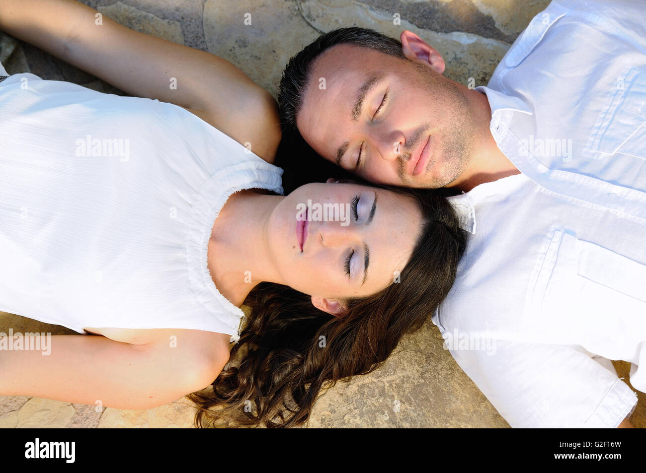 Jeune couple habillé en blanc couché sur un sol en pierre avec les yeux fermé Banque D'Images