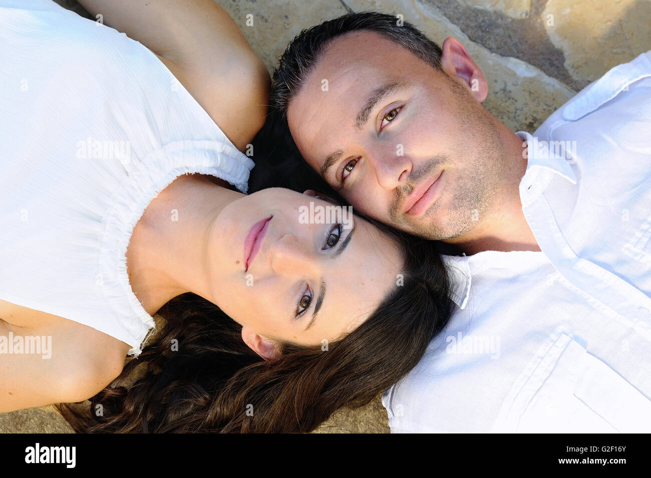 Jeune couple habillé en blanc couché sur un sol en pierre, looking at camera Banque D'Images