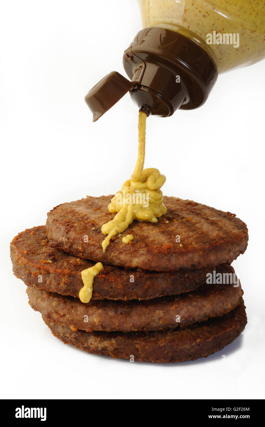La baisse de la bouteille de sauce moutarde sur la viande hachée de bœuf escalope burger Banque D'Images