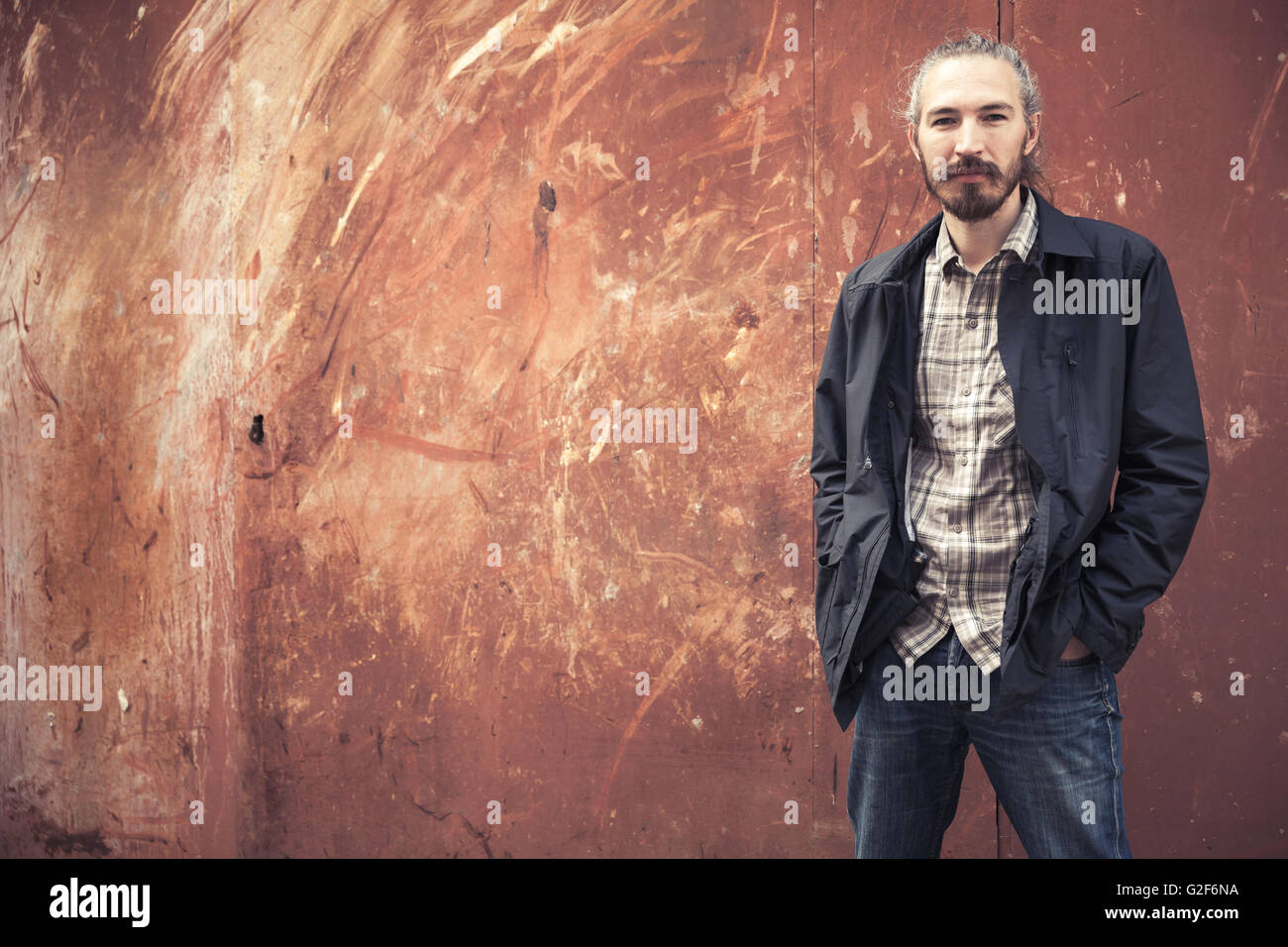 Portrait plein air de jeune homme asiatique barbu dans les tenues sur fond de mur couvert de rouille Banque D'Images