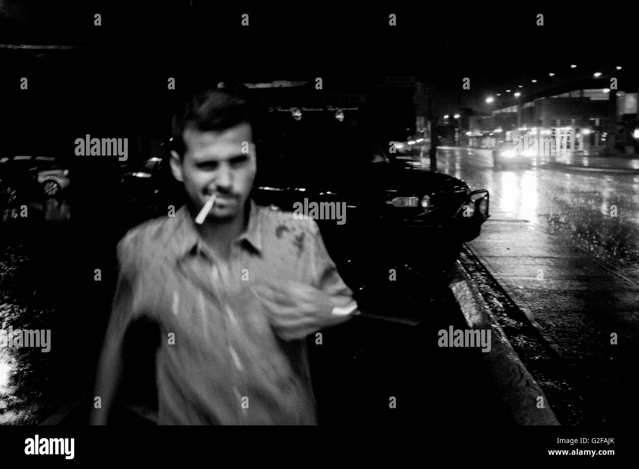 Jeune adulte Homme avec Cigarette en bouche la marche dans la pluie de nuit Banque D'Images