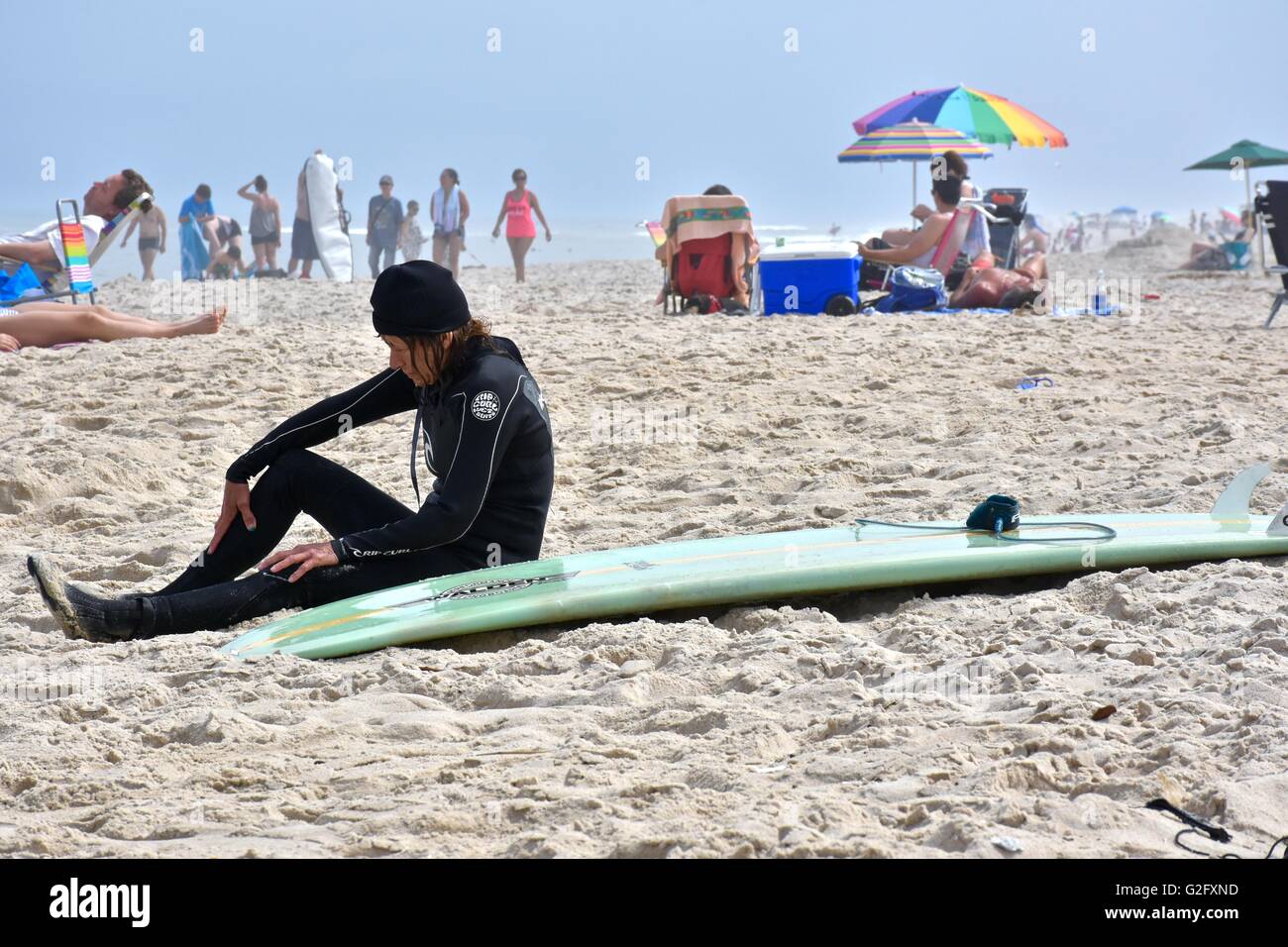 Une femme dans un wet suit assis sur la plage à côté de sa planche de surf Banque D'Images