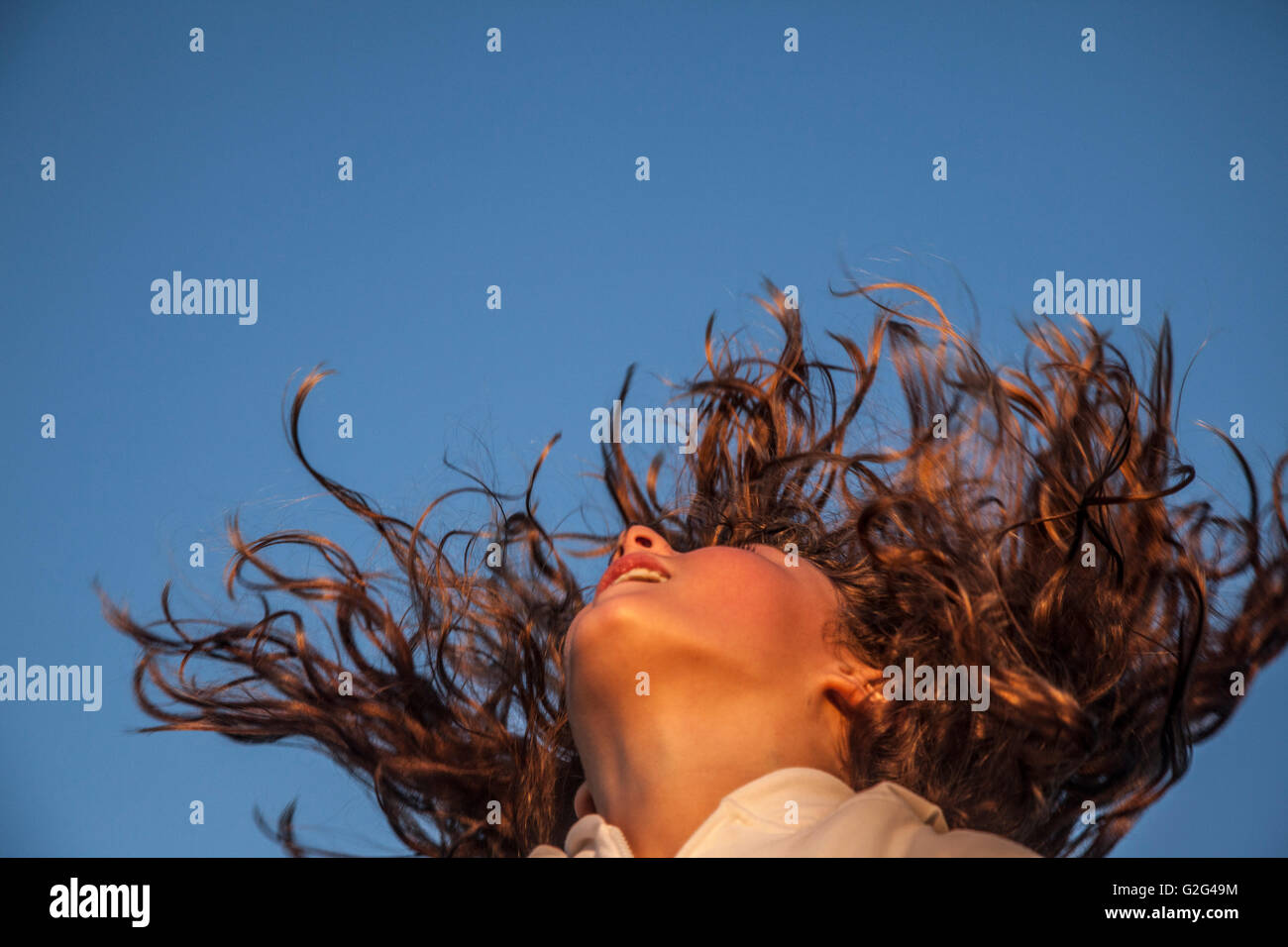 Jeune fille secouant les cheveux bouclés longs Against Blue Sky, Low Angle View Banque D'Images
