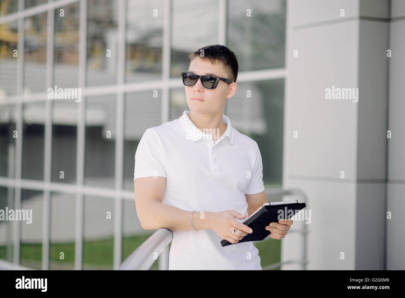 Portrait of a young businessman gardant tablet pc sur la rue. L'homme avec des lunettes et polo blanc. Banque D'Images