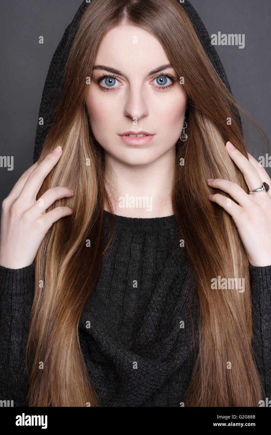 Portrait d'une belle jeune femme aux longs cheveux, magnifique. Elle est vêtue de gris chaud robe tricot avec une capuche. Elle a perfec Banque D'Images