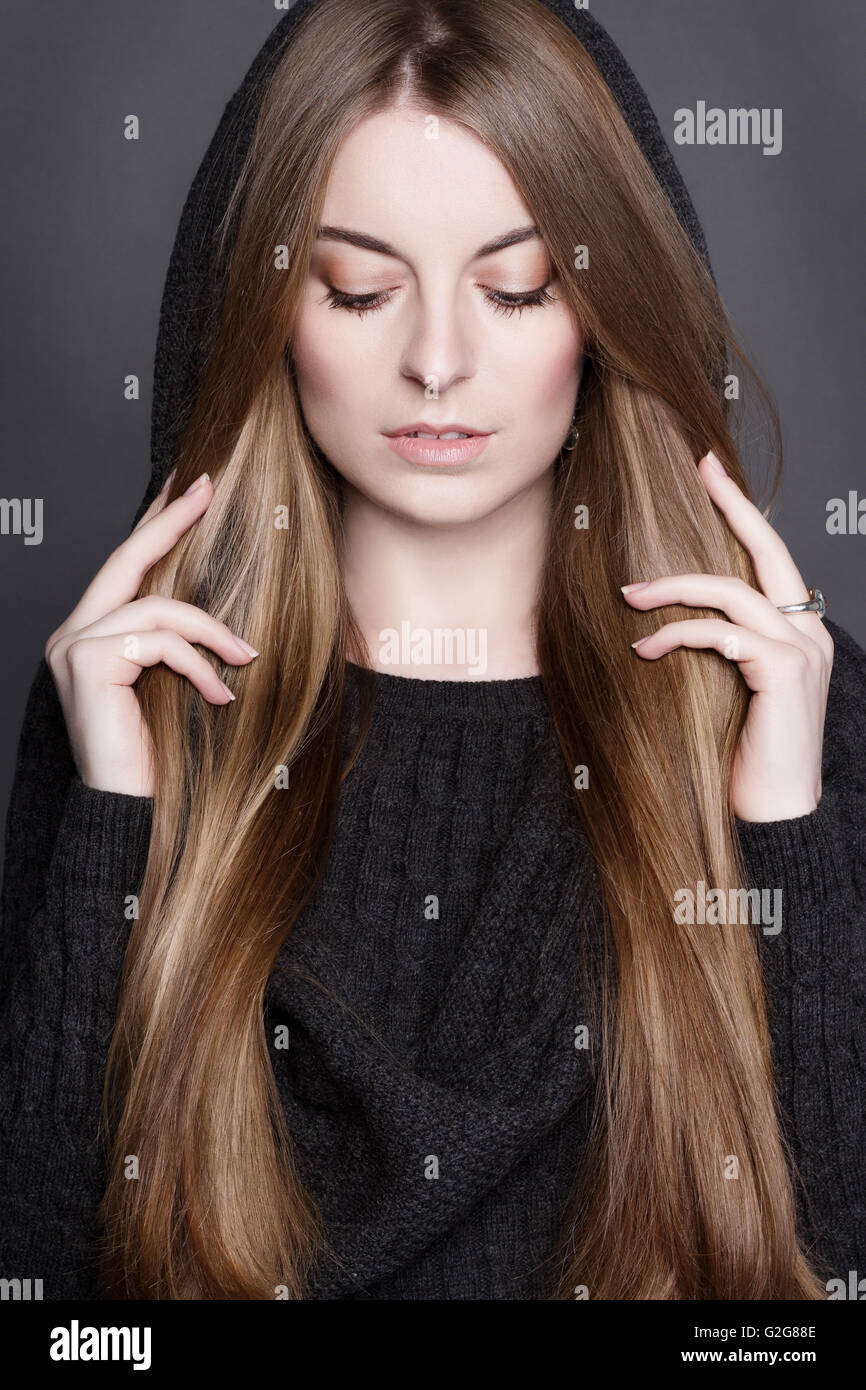 Portrait d'une belle jeune femme aux longs cheveux blond foncé, magnifique. Elle est vêtue de gris chaud robe tricot avec une capuche. Elle Banque D'Images
