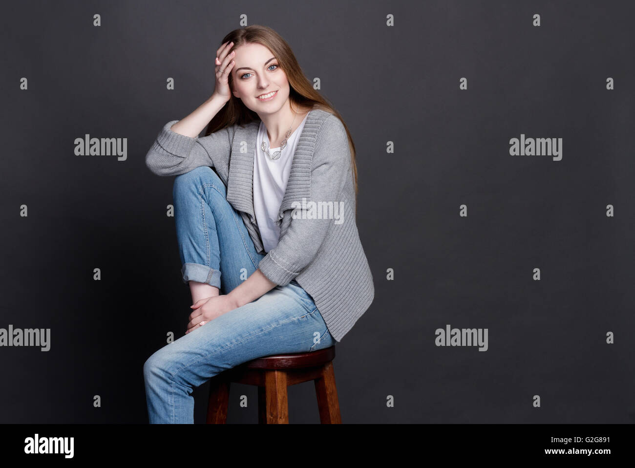 Charmante fille assise sur une chaise en bois. Elle sourit sincèrement. Elle est intelligente et belle, elle est vêtue d'un swea gris Banque D'Images