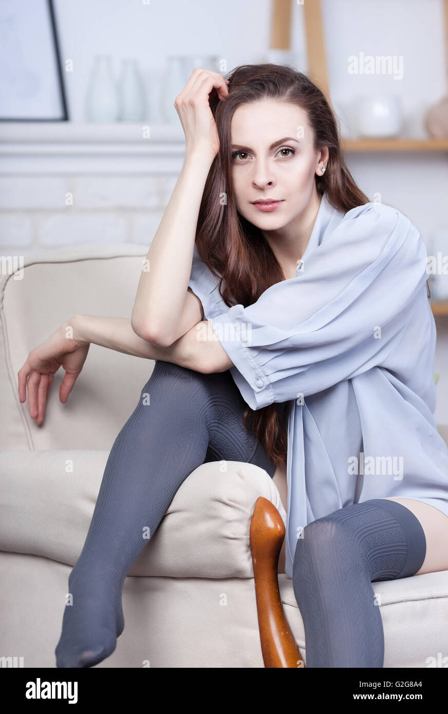 Une jolie jeune femme brune est assise flirty dans un grand fauteuil doux. Elle a de magnifiques cheveux noirs et la peau pâle. Elle porte stocki Banque D'Images