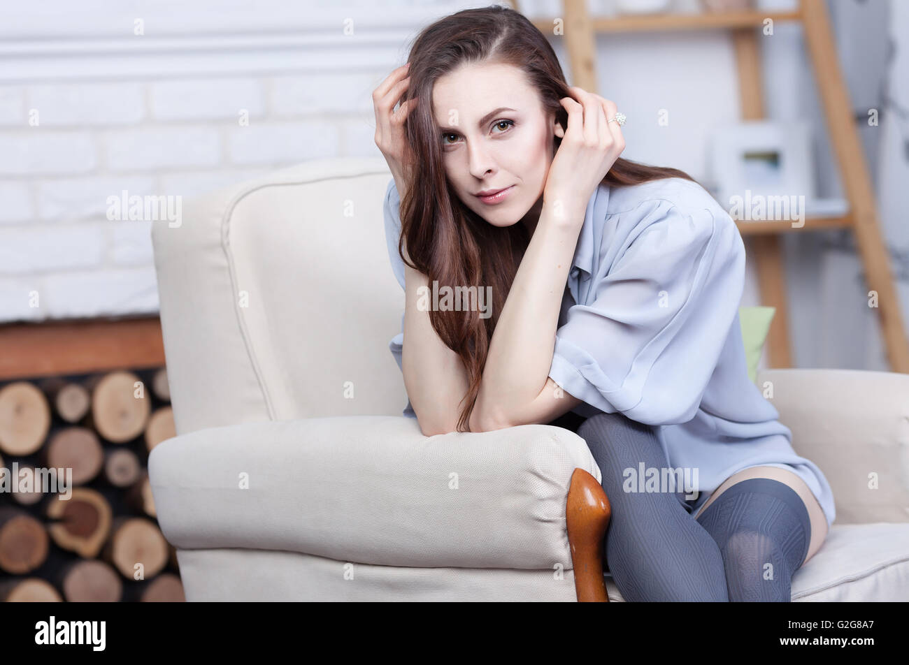 Une jolie jeune femme brune est assise flirty dans un grand fauteuil doux. Elle a de magnifiques cheveux noirs et la peau pâle. Elle porte stocki Banque D'Images