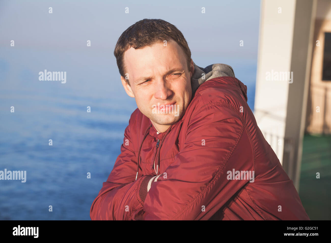 Beau jeune homme de race blanche debout sur le pont à pied de navire de croisière en soirée lumineuse du soleil Banque D'Images