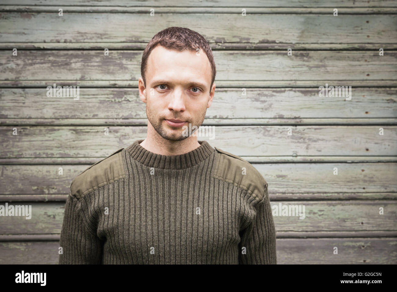 Beau jeune homme de race blanche dans chandail vert militaire. Piscine close up portrait sur green rural mur en bois Banque D'Images
