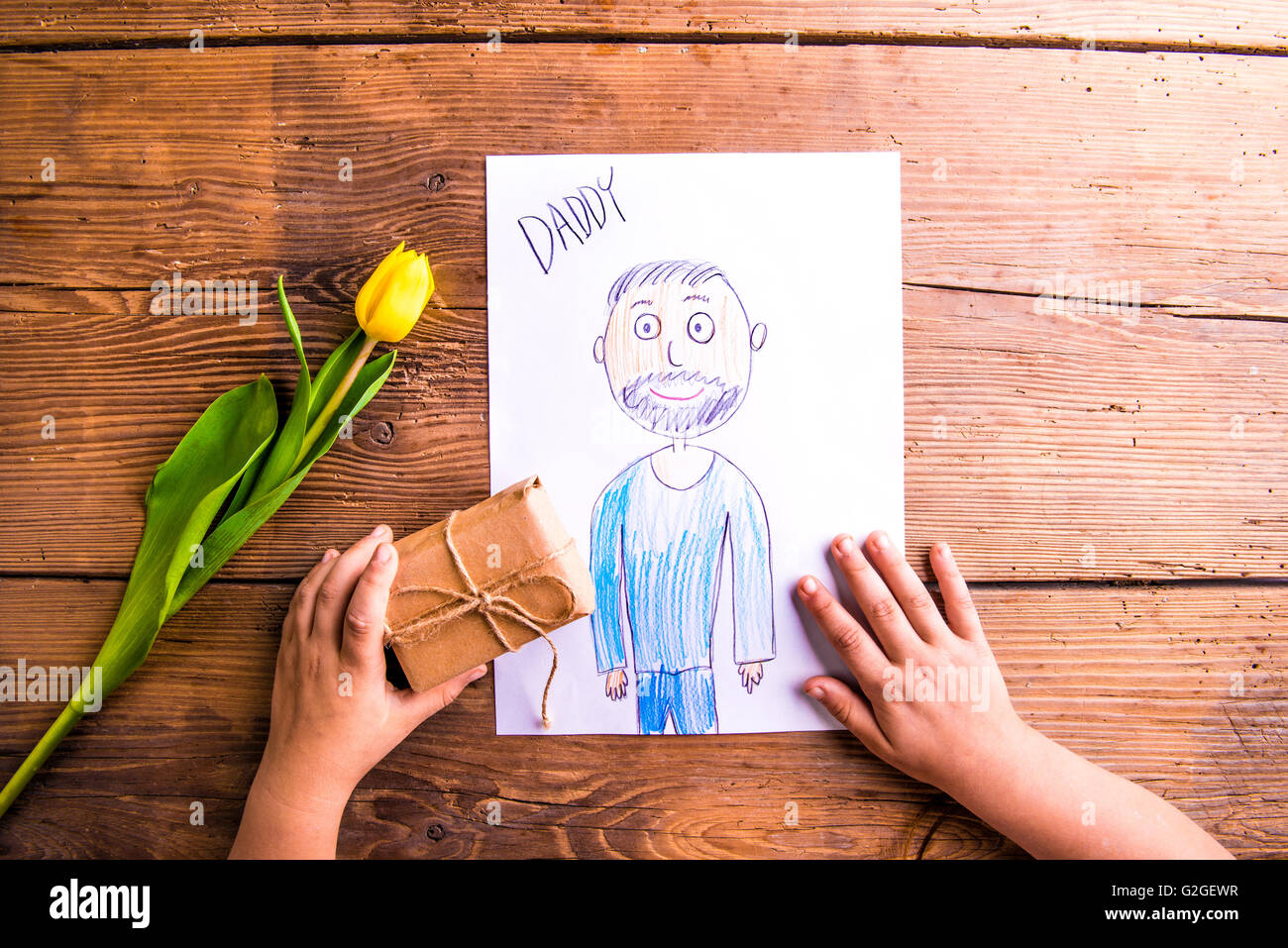 Composition des pères. Mains d'enfant tenant un dessin méconnaissable de son père et de son petit cadeau. Tulipe jaune. Sho Studio Banque D'Images