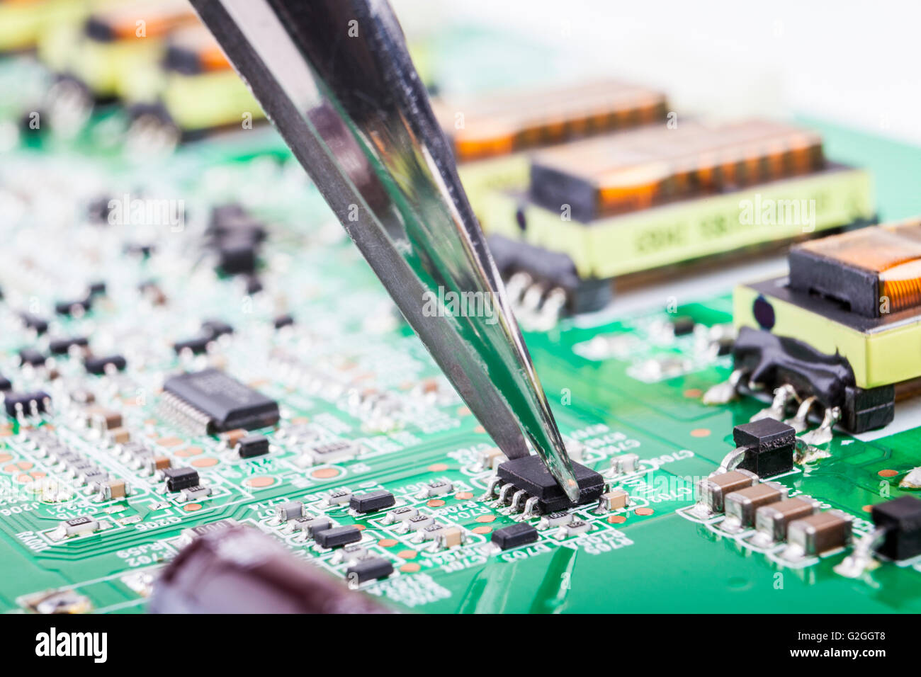 Petits composants électroniques avec pince à épiler sur carte de circuit imprimé verte Banque D'Images