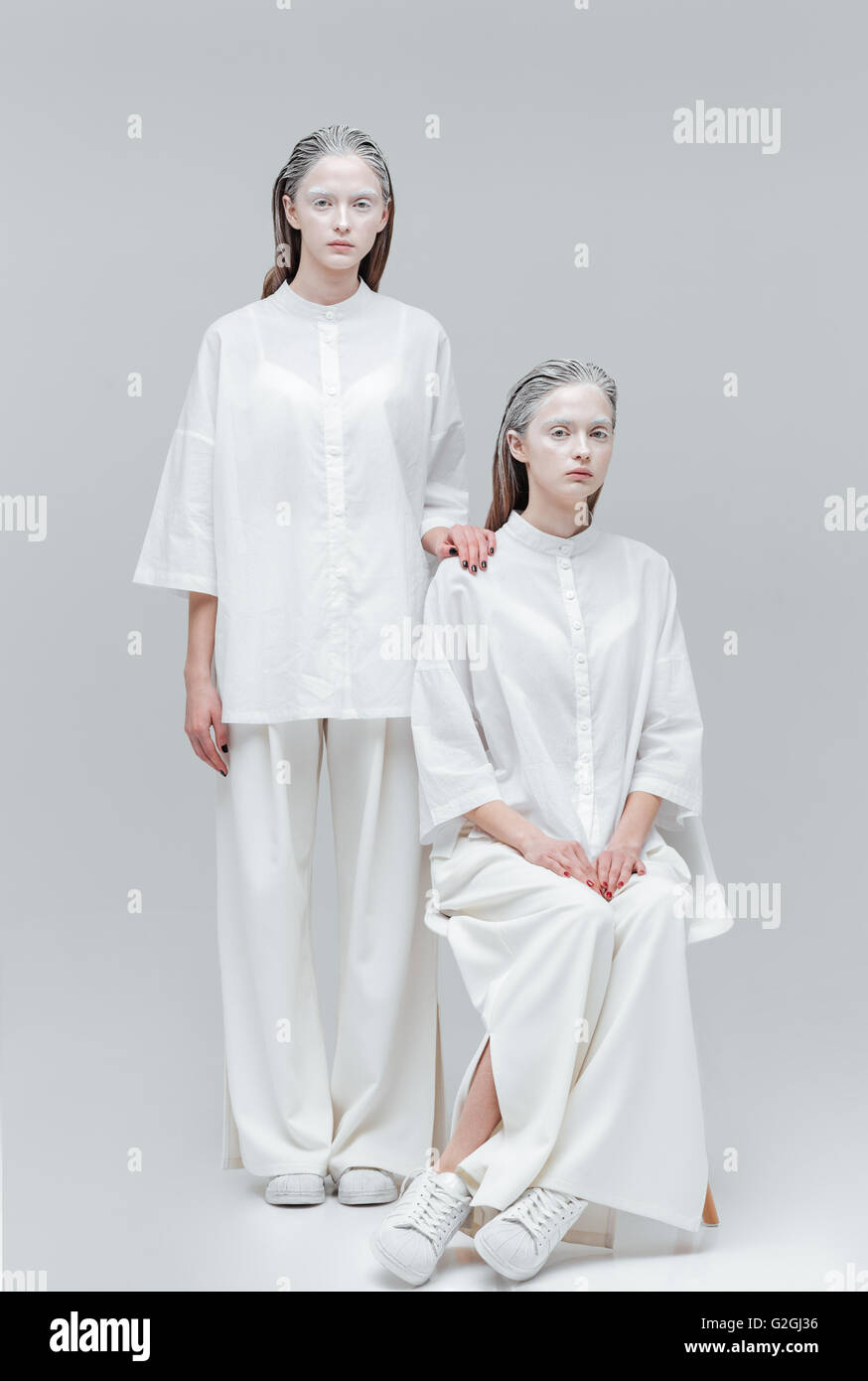 Deux belles mode filles portant des vêtements blancs isolés sur gray Banque D'Images