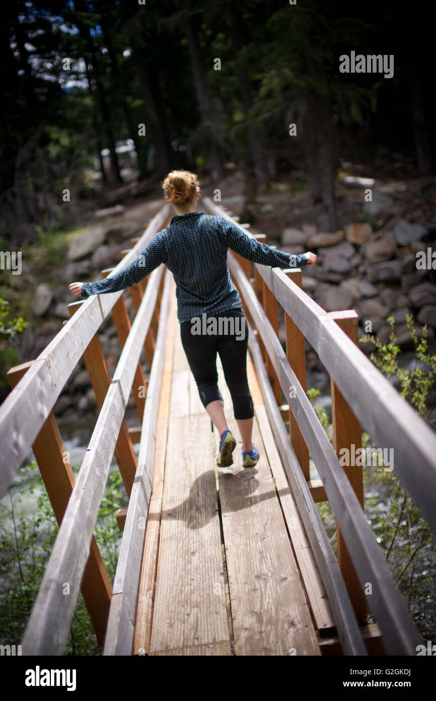 Young Adult Woman Crossing passerelle en Forêt, Vue arrière Banque D'Images