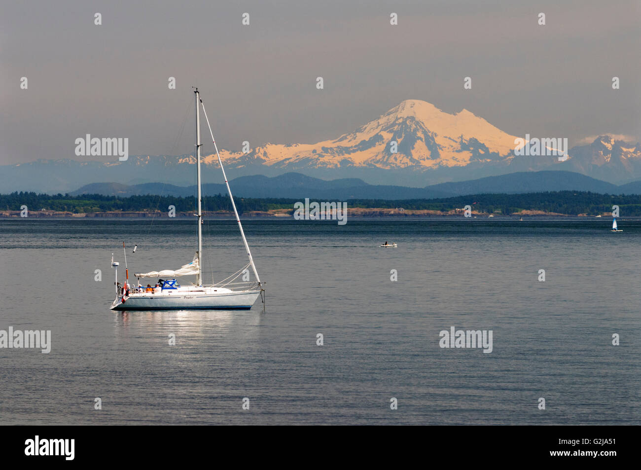 Un voilier au large de la plage de saules à Oak Bay à Victoria, en Colombie-Britannique. Dans l'arrière-plan est Mt. Baker dans l'État de Washington, USA. Banque D'Images