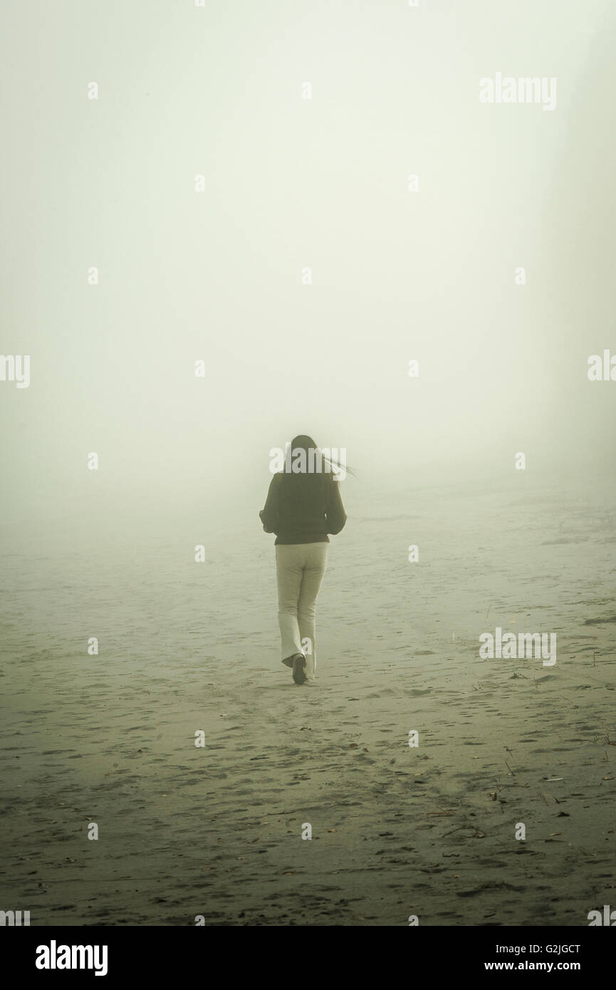Femme marche dans la brume sur une plage de sable fin Banque D'Images