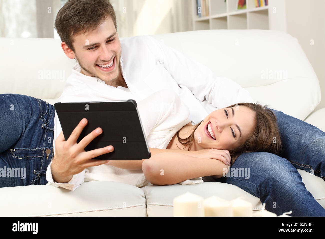 Couple heureux de regarder du contenu multimédia dans un comprimé couché dans un canapé à la maison Banque D'Images