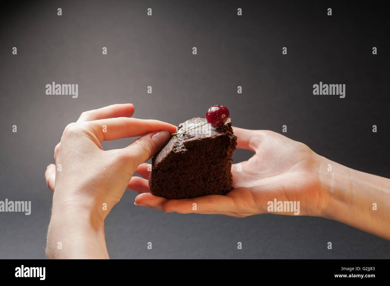 Tranche de délicieux gâteau au chocolat avec cerise sur le gâteau dans les mains d'une femme sur un fond sombre. Banque D'Images