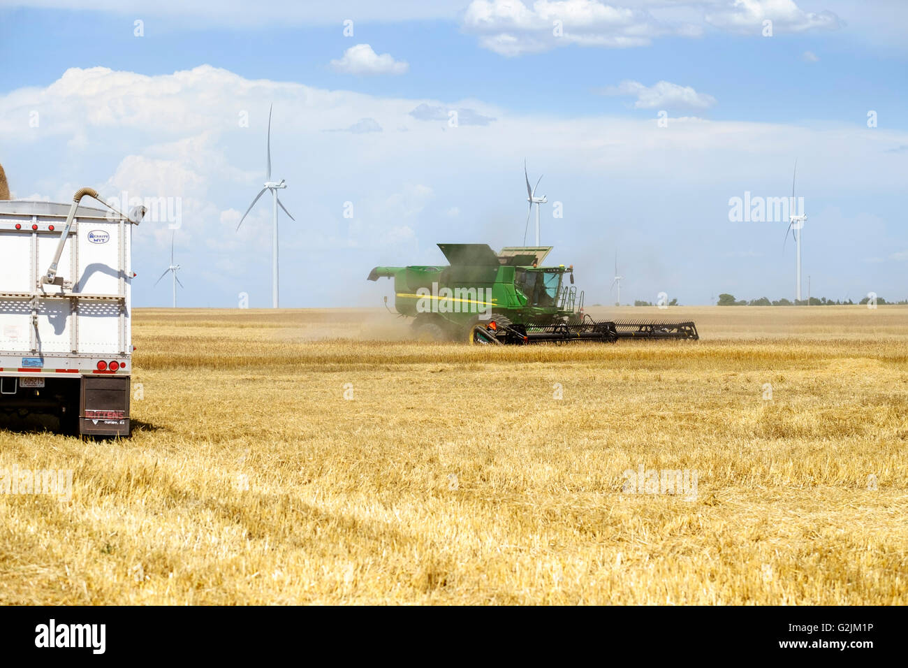 Une moissonneuse-batteuse John Deere blé récoltes tout en un se distingue par grain semi pour chargement dans l'Oklahoma, USA. Ferme éolienne en arrière-plan. Banque D'Images