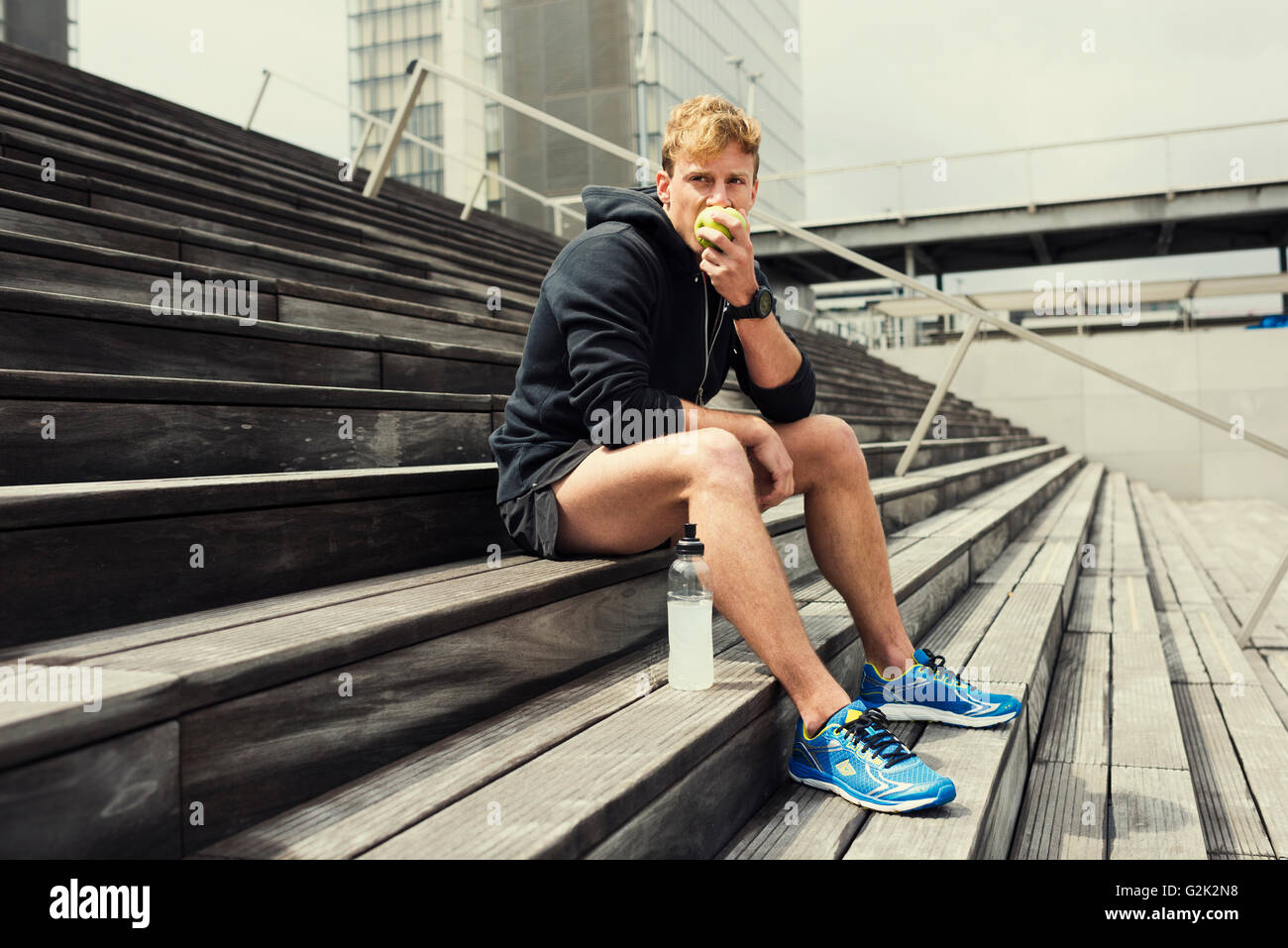 Manger un jogger urbain green apple après l'entraînement. Arrière-plan de la ville Banque D'Images