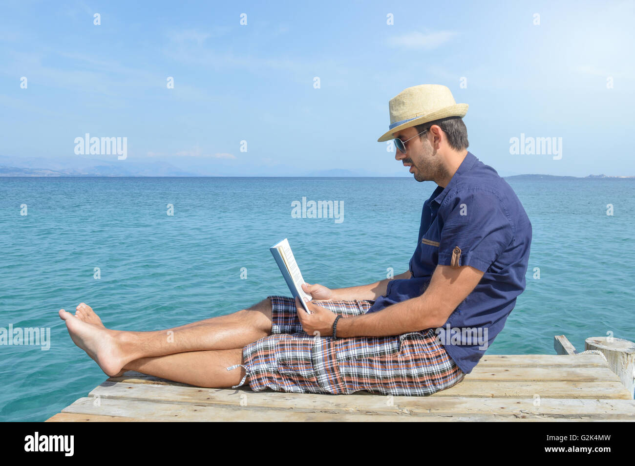 L'homme en chemise bleue assis sur le quai, la lecture d'un livre Banque D'Images