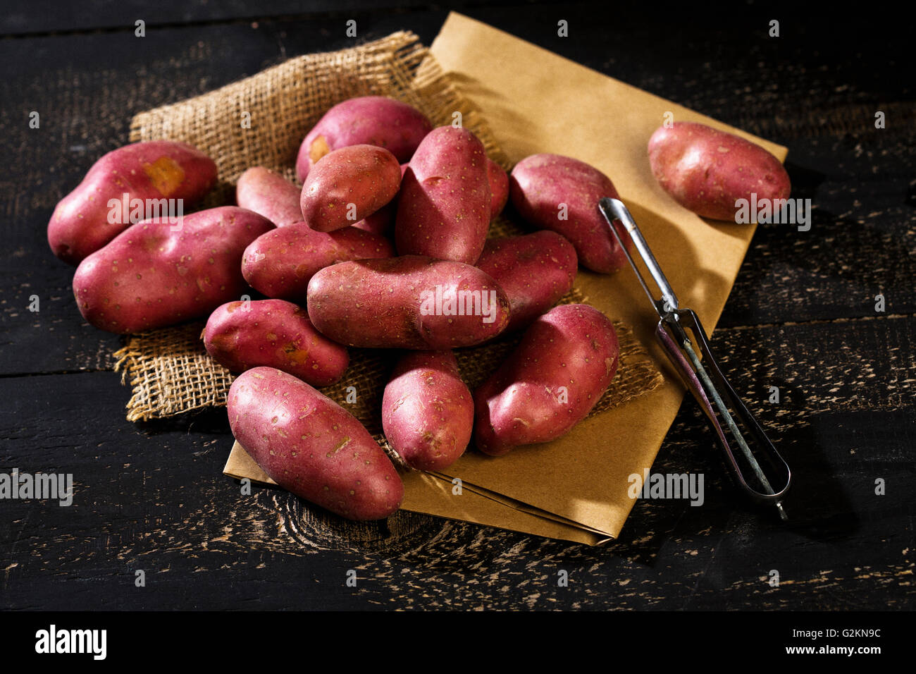 Pommes de terre grenaille brute et peeler sur du papier brun, le jute et le bois foncé Banque D'Images