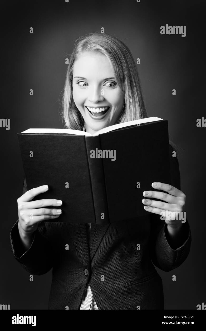Jolie jeune modèle qui tient à la lecture est la tenue d'un livre bleu ouvert en face d'elle, gardant le livre près de son visage ensemble exp Banque D'Images