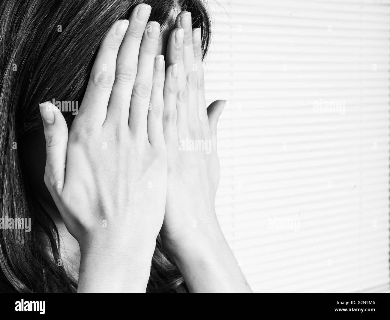 Portrait noir et blanc d'une jeune femme couvrant son visage dans la honte ou l'embarras Banque D'Images