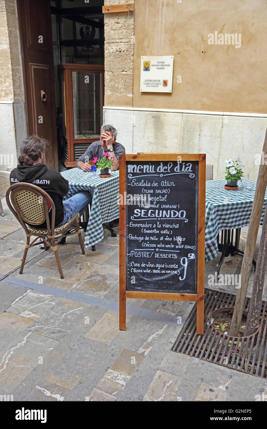 Deux hommes assis à table à côté de blackboard menu restaurant à l'extérieur, Alcudia, Majorque Banque D'Images